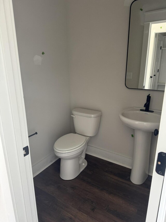 half bath with baseboards, toilet, and wood finished floors