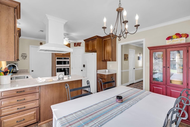 kitchen featuring island exhaust hood, crown molding, sink, white appliances, and ceiling fan with notable chandelier