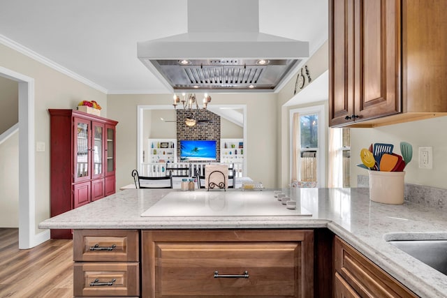 kitchen featuring exhaust hood, an inviting chandelier, light hardwood / wood-style floors, light stone countertops, and crown molding