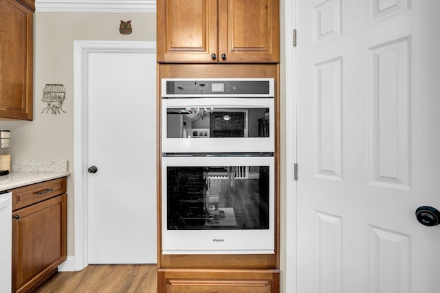 kitchen featuring light stone countertops, crown molding, light hardwood / wood-style floors, and white appliances