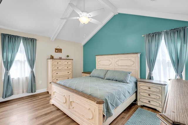 bedroom featuring ceiling fan, multiple windows, hardwood / wood-style floors, and vaulted ceiling with beams