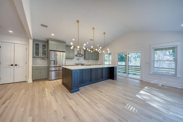 kitchen featuring stainless steel fridge with ice dispenser, light countertops, lofted ceiling, an inviting chandelier, and wall chimney exhaust hood