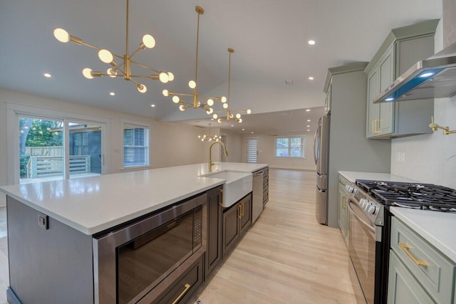 kitchen with an inviting chandelier, lofted ceiling, a sink, stainless steel appliances, and wall chimney exhaust hood