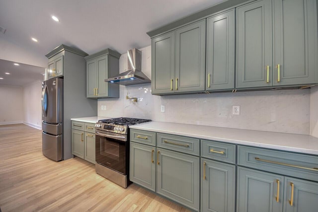 kitchen featuring wall chimney range hood, appliances with stainless steel finishes, light wood finished floors, decorative backsplash, and light countertops