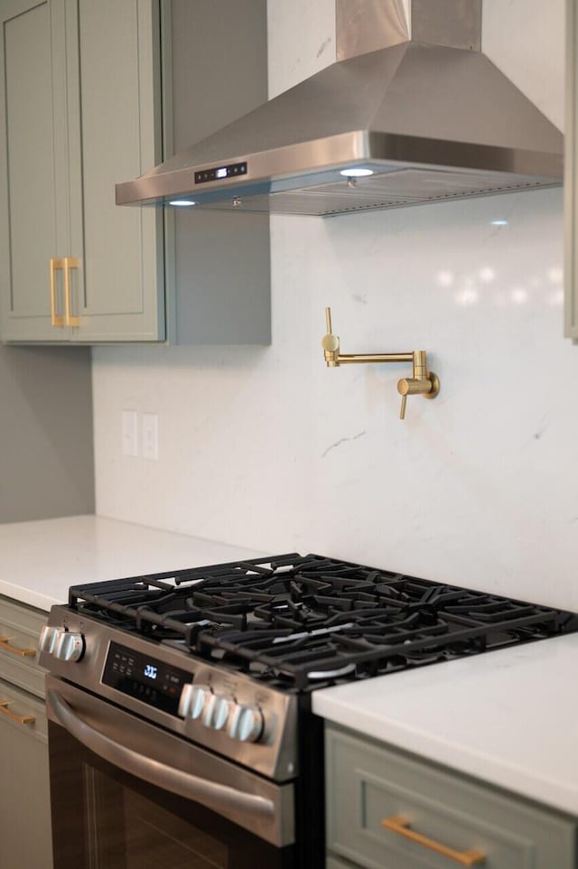 kitchen featuring gray cabinetry, backsplash, wall chimney exhaust hood, light countertops, and gas range