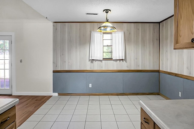 unfurnished dining area featuring a textured ceiling, wooden walls, and light hardwood / wood-style flooring