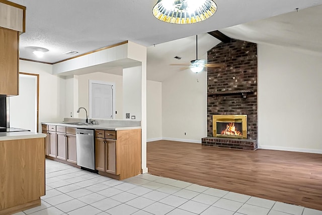 kitchen featuring a brick fireplace, stainless steel dishwasher, sink, vaulted ceiling with beams, and light hardwood / wood-style floors