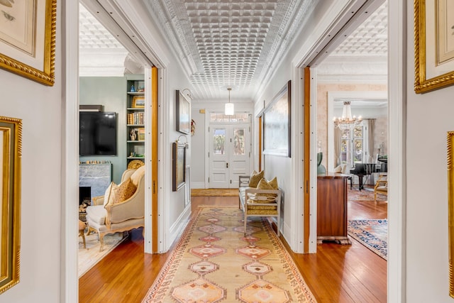 corridor with crown molding, a chandelier, built in shelves, and light wood-type flooring