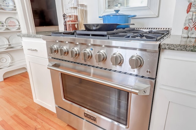 interior details featuring high end stove, white cabinets, light hardwood / wood-style flooring, and stone counters