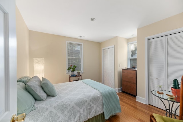 bedroom with multiple closets, visible vents, baseboards, and wood finished floors