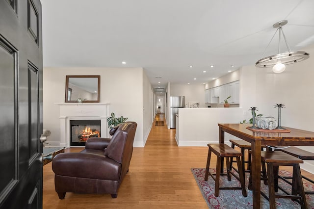 dining room featuring a glass covered fireplace, light wood-style flooring, baseboards, and recessed lighting