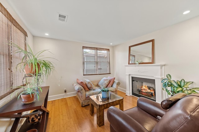 living room featuring light wood-style floors, visible vents, a lit fireplace, and baseboards