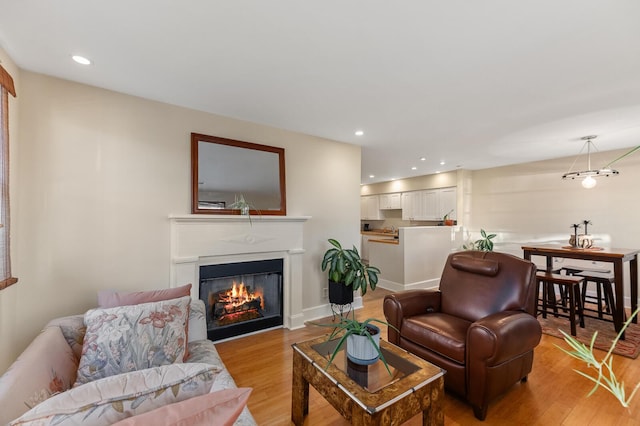 living room with baseboards, a glass covered fireplace, light wood-style flooring, and recessed lighting