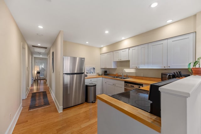 kitchen featuring wood counters, freestanding refrigerator, light wood-style floors, black microwave, and a sink