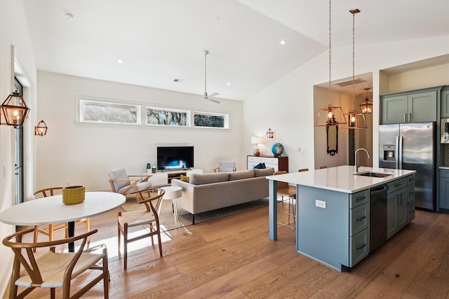 kitchen with appliances with stainless steel finishes, ceiling fan with notable chandelier, sink, light hardwood / wood-style floors, and an island with sink