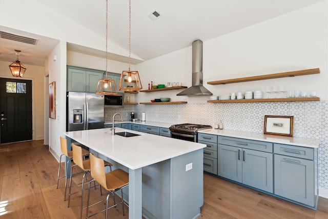 kitchen featuring hanging light fixtures, sink, stainless steel appliances, and wall chimney range hood