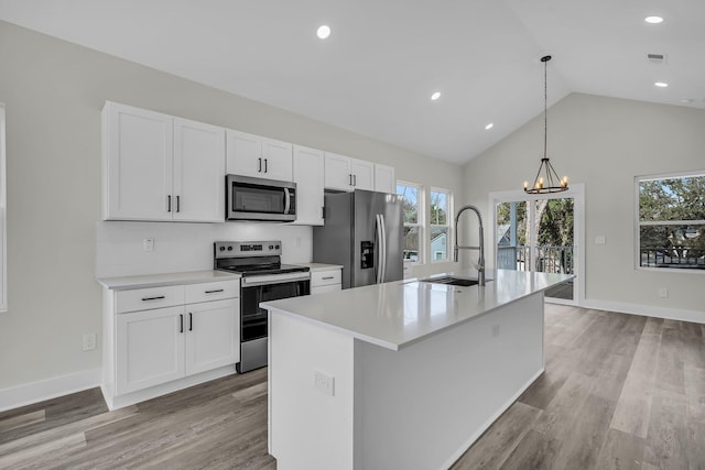 kitchen with stainless steel appliances, light countertops, hanging light fixtures, white cabinets, and a kitchen island with sink