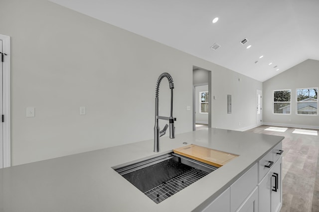 kitchen featuring open floor plan, vaulted ceiling, light countertops, white cabinetry, and a sink