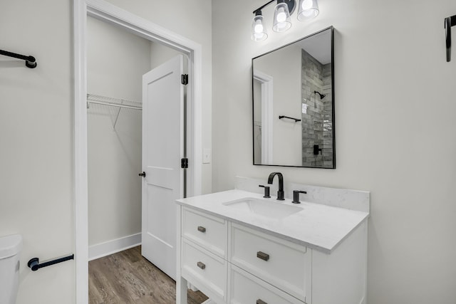 bathroom featuring toilet, a walk in closet, wood finished floors, and vanity