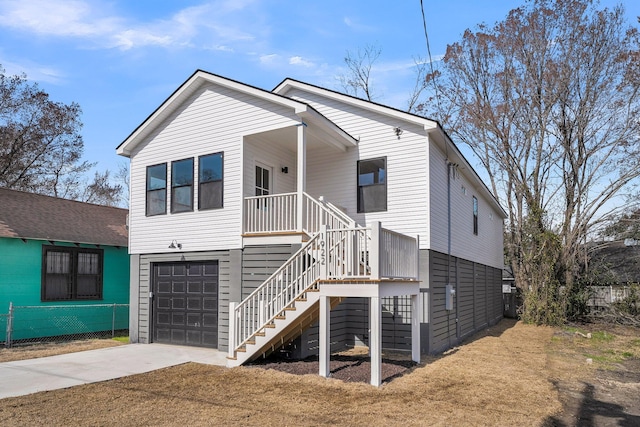 coastal inspired home with a porch, concrete driveway, stairway, fence, and a garage