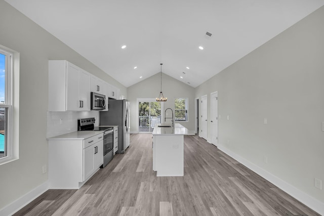 kitchen with a center island with sink, appliances with stainless steel finishes, light countertops, pendant lighting, and a sink