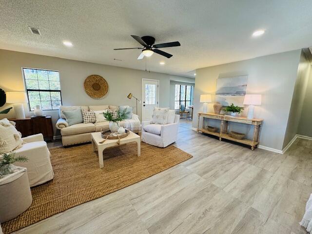 living room featuring ceiling fan, light hardwood / wood-style floors, and a textured ceiling