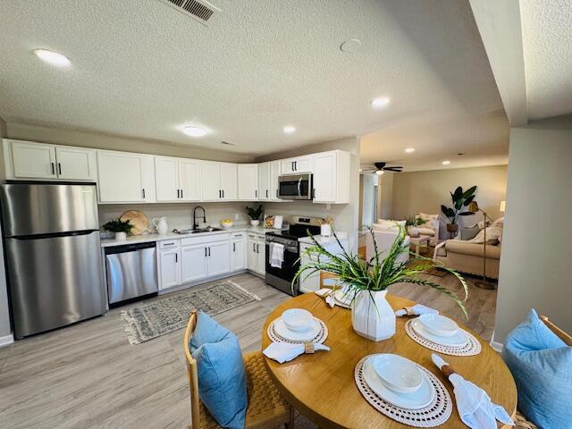 dining space with a textured ceiling, light hardwood / wood-style floors, ceiling fan, and sink