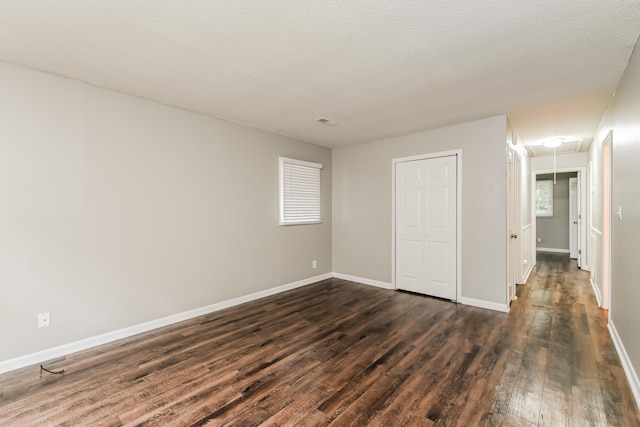 unfurnished bedroom with a textured ceiling, dark wood-type flooring, and a closet