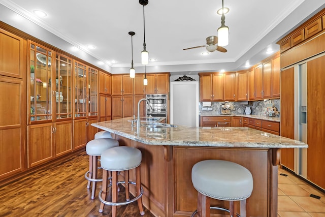 kitchen with pendant lighting, decorative backsplash, ornamental molding, and a center island with sink