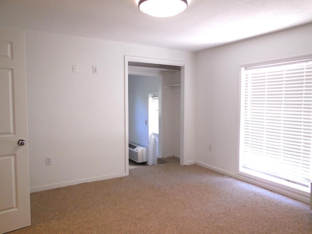 empty room featuring a textured ceiling, a wall unit AC, and light colored carpet