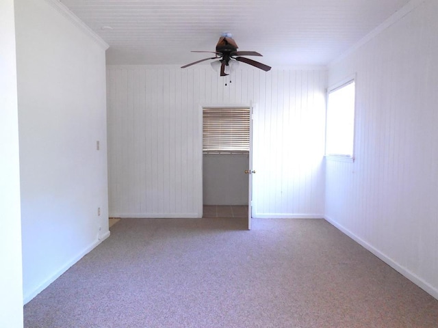 carpeted empty room with crown molding, ceiling fan, and wooden walls