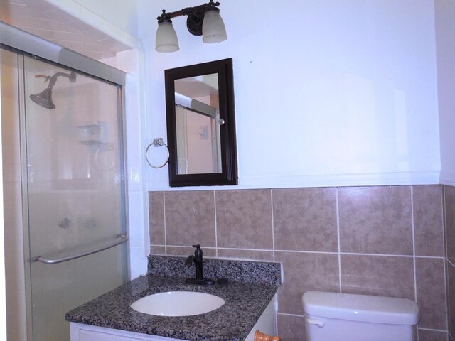 bathroom featuring walk in shower, tile walls, vanity, and toilet