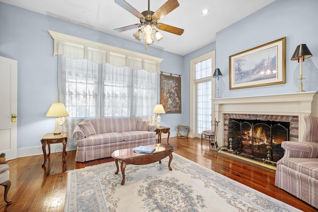 living room with a brick fireplace, ceiling fan, and wood-type flooring