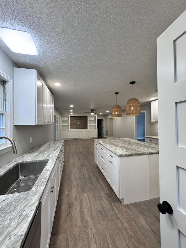 kitchen featuring dark hardwood / wood-style floors, decorative light fixtures, white cabinetry, sink, and light stone counters