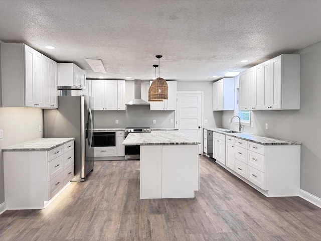 kitchen with wall chimney range hood, stainless steel appliances, white cabinets, a kitchen island, and decorative light fixtures