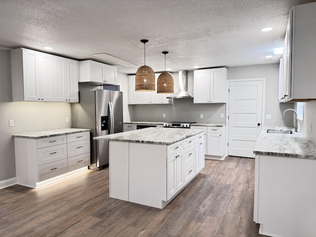 kitchen with wall chimney range hood, a center island, stainless steel refrigerator with ice dispenser, white cabinets, and decorative light fixtures