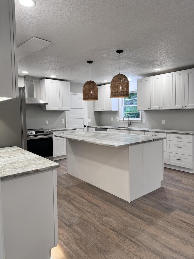 kitchen with white cabinets, a center island, wall chimney exhaust hood, and appliances with stainless steel finishes