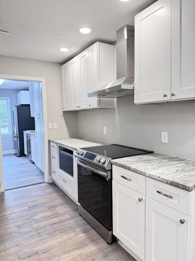 kitchen with wall chimney exhaust hood, white cabinetry, light hardwood / wood-style flooring, appliances with stainless steel finishes, and light stone countertops