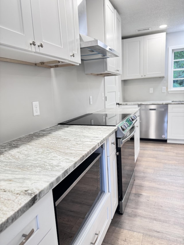 kitchen featuring white cabinetry, light stone counters, stainless steel appliances, light hardwood / wood-style floors, and wall chimney range hood