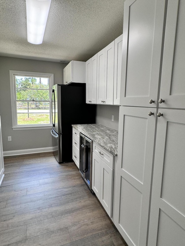 kitchen featuring white cabinets, beverage cooler, light stone countertops, a textured ceiling, and light wood-type flooring