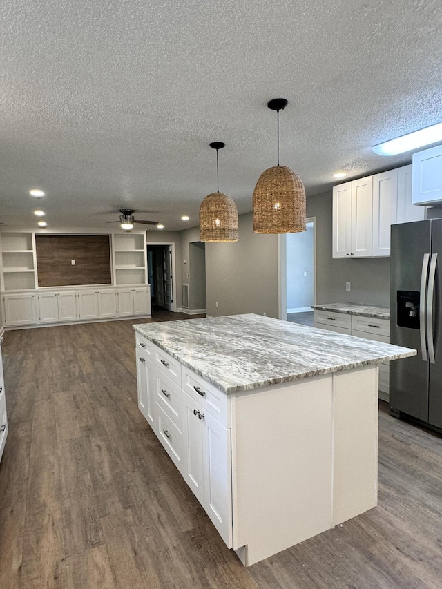 kitchen with a kitchen island, white cabinetry, stainless steel fridge, hanging light fixtures, and light stone countertops