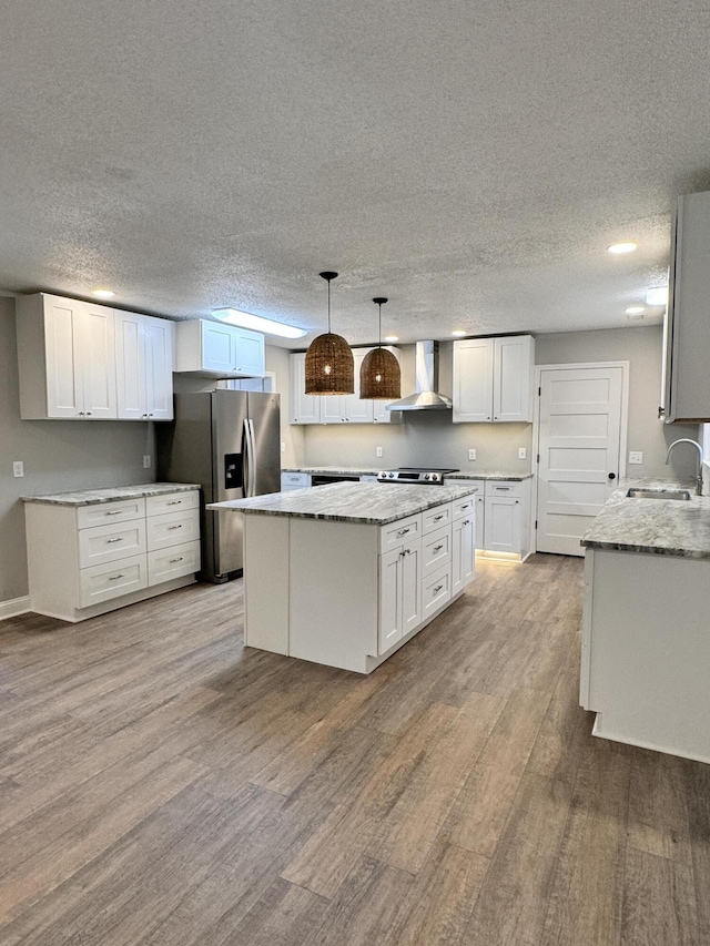 kitchen featuring pendant lighting, sink, white cabinets, a center island, and wall chimney range hood