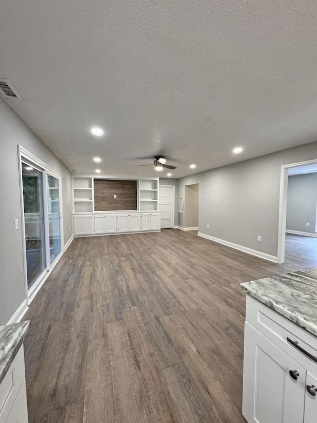 unfurnished living room with dark wood-type flooring, ceiling fan, built in shelves, and a textured ceiling