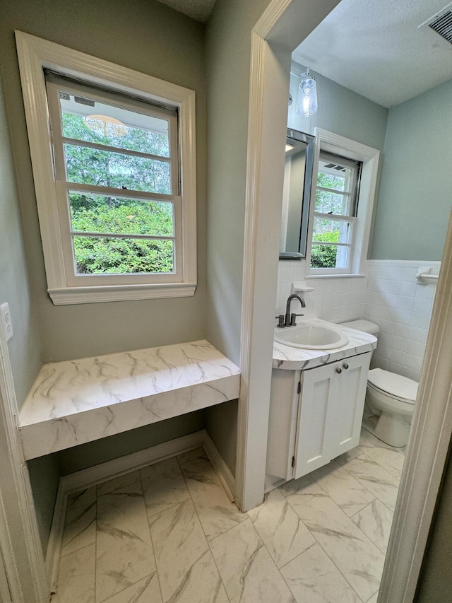 bathroom with vanity, toilet, a textured ceiling, and tile walls