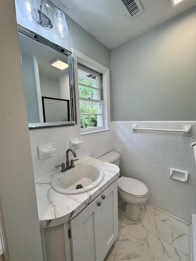 bathroom featuring vanity, tile walls, toilet, and a textured ceiling