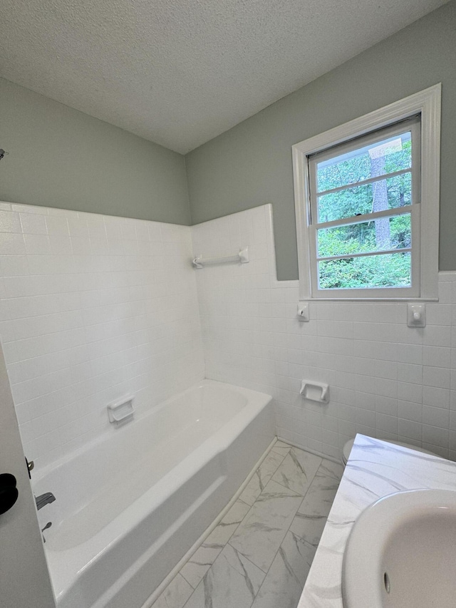 bathroom with a tub, sink, tile walls, and a textured ceiling