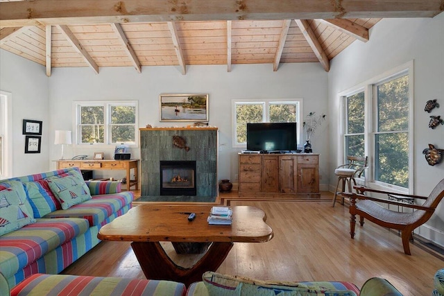 living room featuring beam ceiling, high vaulted ceiling, a tile fireplace, and light wood-type flooring