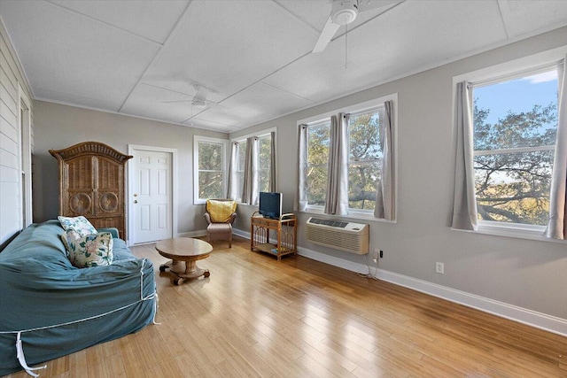 sitting room with ceiling fan, a paneled ceiling, light wood-type flooring, and an AC wall unit