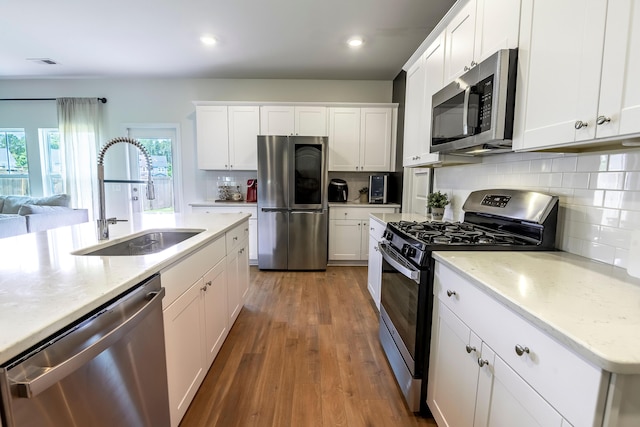 kitchen featuring appliances with stainless steel finishes, a sink, backsplash, white cabinets, and wood finished floors