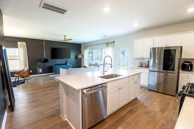 kitchen with appliances with stainless steel finishes, a sink, light countertops, a kitchen island with sink, and white cabinets